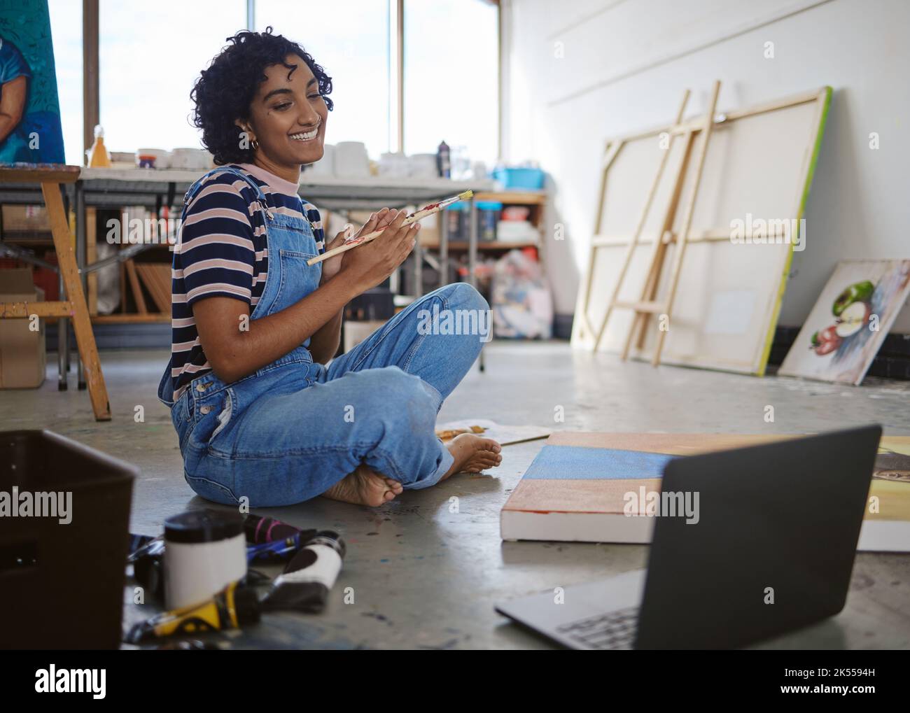 Malen, Kunst und Laptop mit einer Malerin nach einem Internetkurs in ihrer Kreativwerkstatt oder ihrem Atelier. Computer, Malerei und künstlerisch mit einem Stockfoto