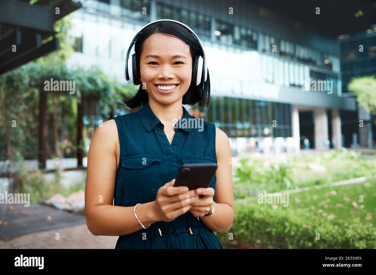 Asiatische Frau, Kopfhörer und Telefon, während sie Musik, Videos oder Podcasts streamen, die draußen in der Pause stehen und sich frei und glücklich im Internet fühlen. Hochformat und Stockfoto