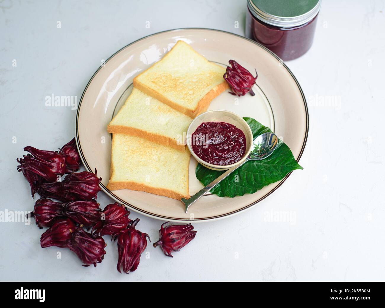 Hibiskusmarmelade und Toasts gegen das Glas mit Marmelade und Hibiskusblüten Stockfoto