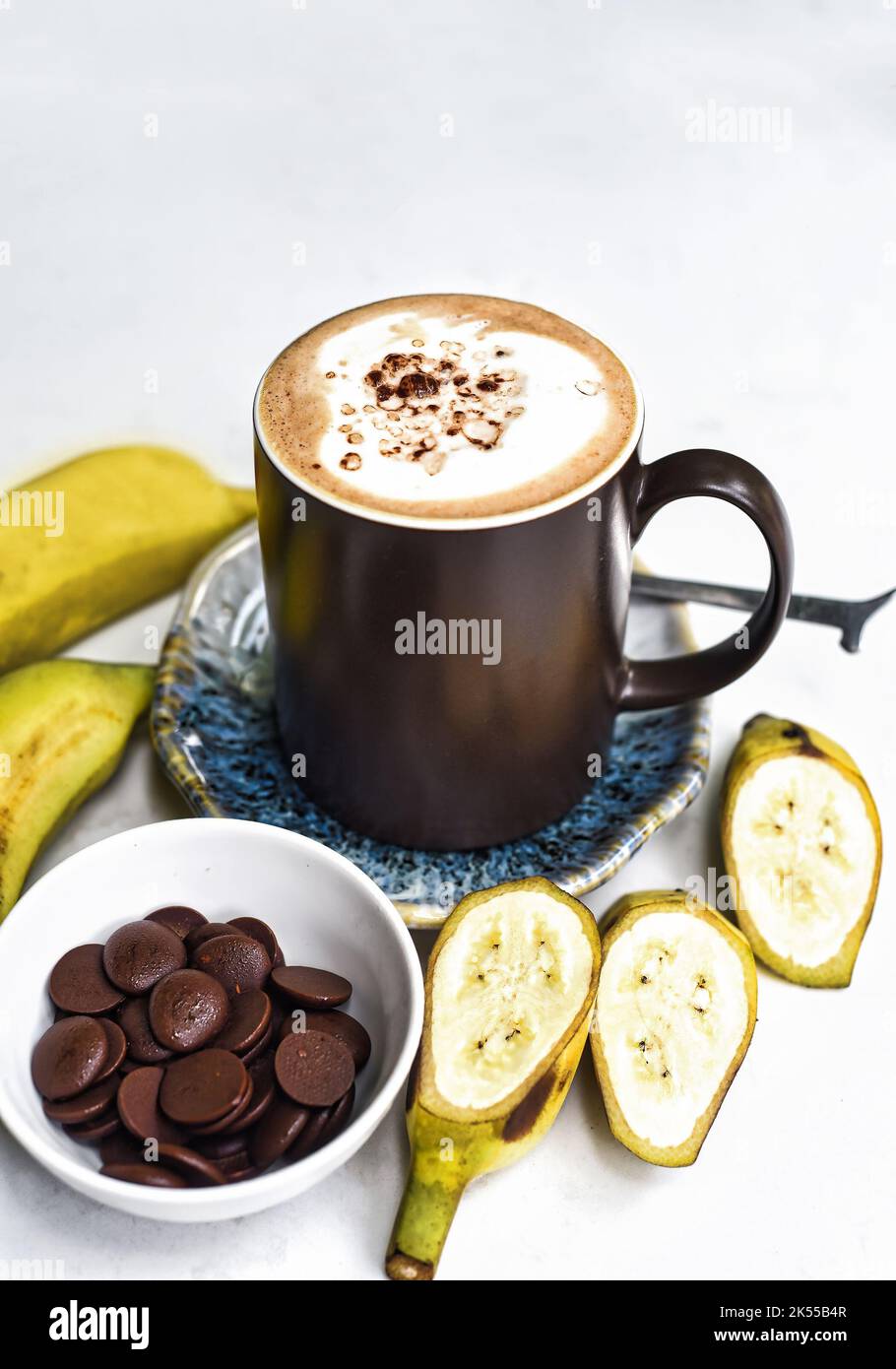 Bananenschokolade-Latte mit frischen Bananen- und Schokoladentropfen auf weißem Tisch Stockfoto