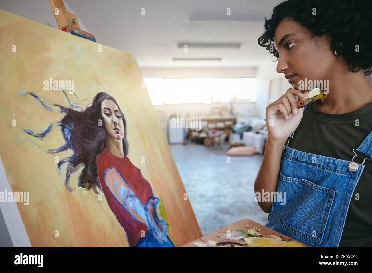 Eine kreative Frau, die über ihre Kunst nachdenkt und sich die Malerei im Atelier zur Ausstellung ansieht. Professioneller indischer Maler, Künstler mit Pinsel, Suche Stockfoto