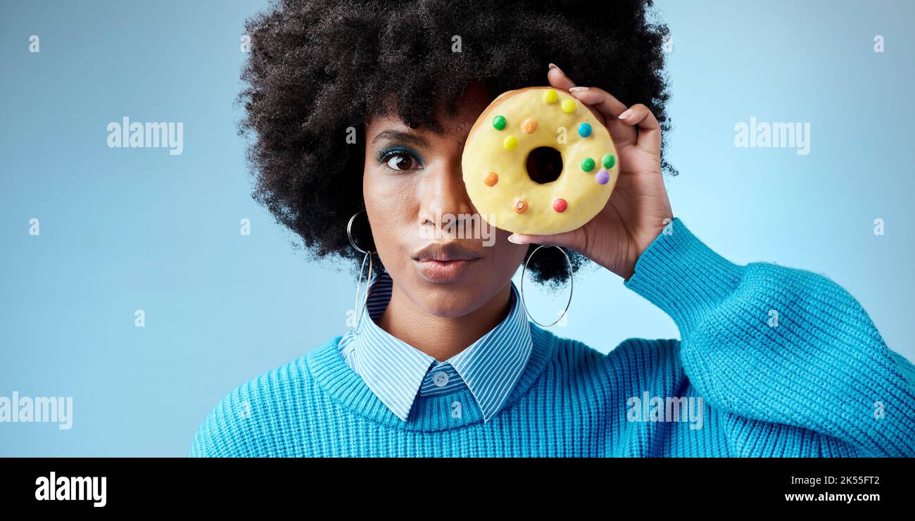 Schönheit, schwarze Frau und Donut Porträt über Gesicht, Feier von Afrika und süßen Stil auf dem Auge mit blauem Hintergrund. Mode, afrikanisches Model und Kuchen Stockfoto