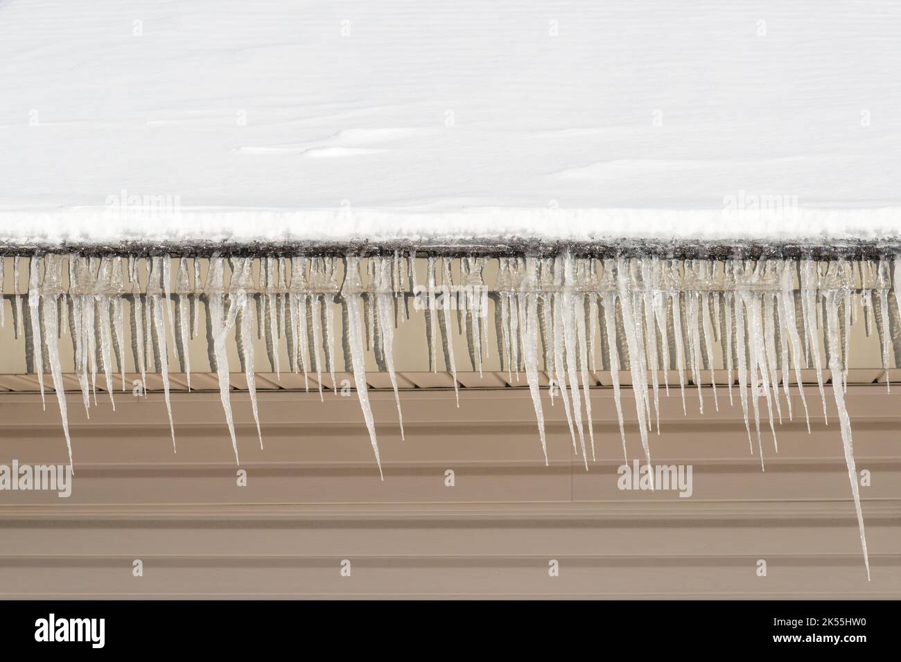 Eiszapfen, die an einem Wintertag von einem schneebedeckten Dach hängen. Platz für Text oben oder unten. Stockfoto