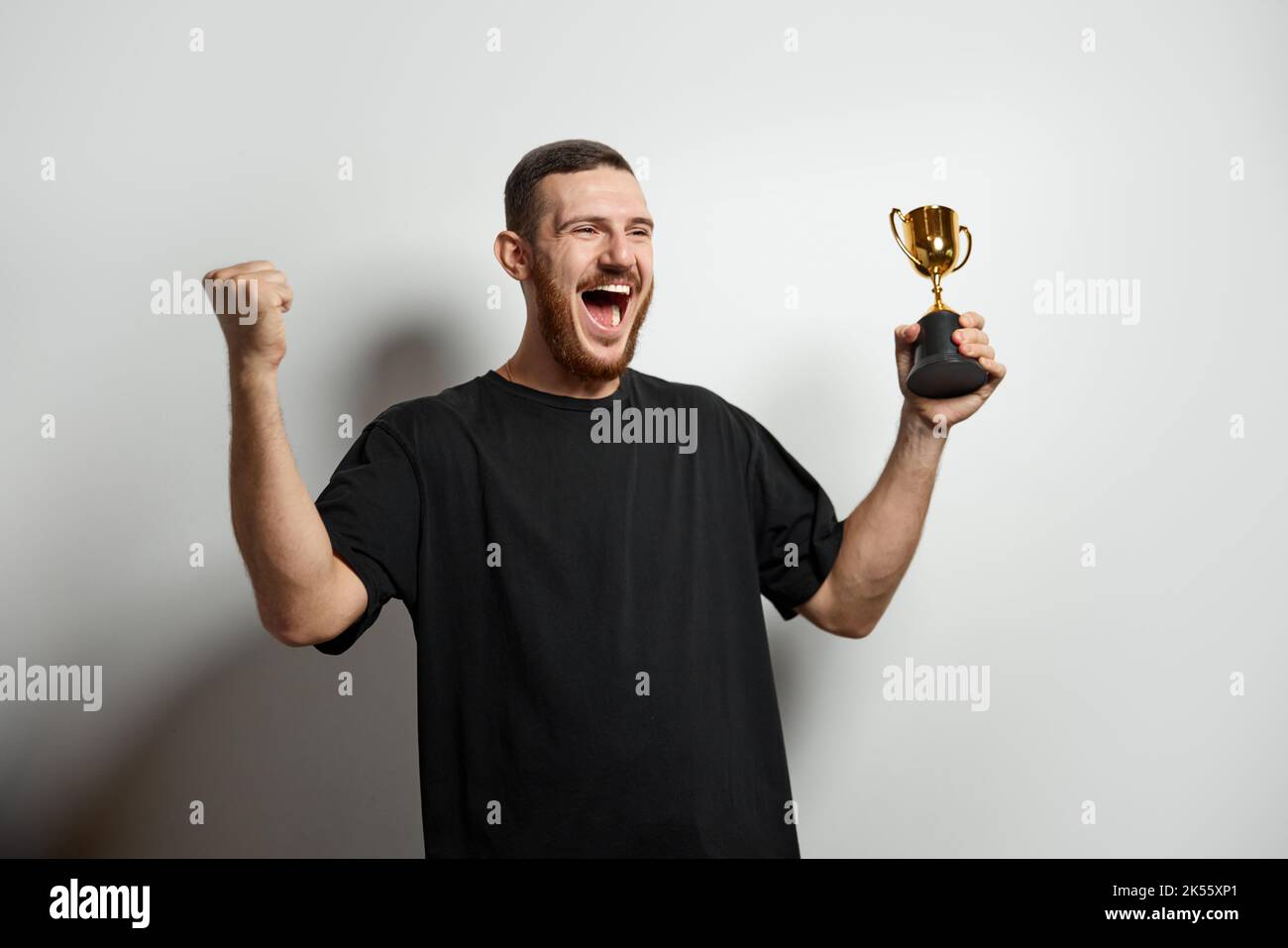 Glücklicher junger Mann oder Geschäftsmann, der seine Goldtrophäe hält und den Sieg feiert. Studioaufnahme eines Mannes mit Pokal als Sieger. Konzept von Sieg, Erfolg, Mensch Stockfoto