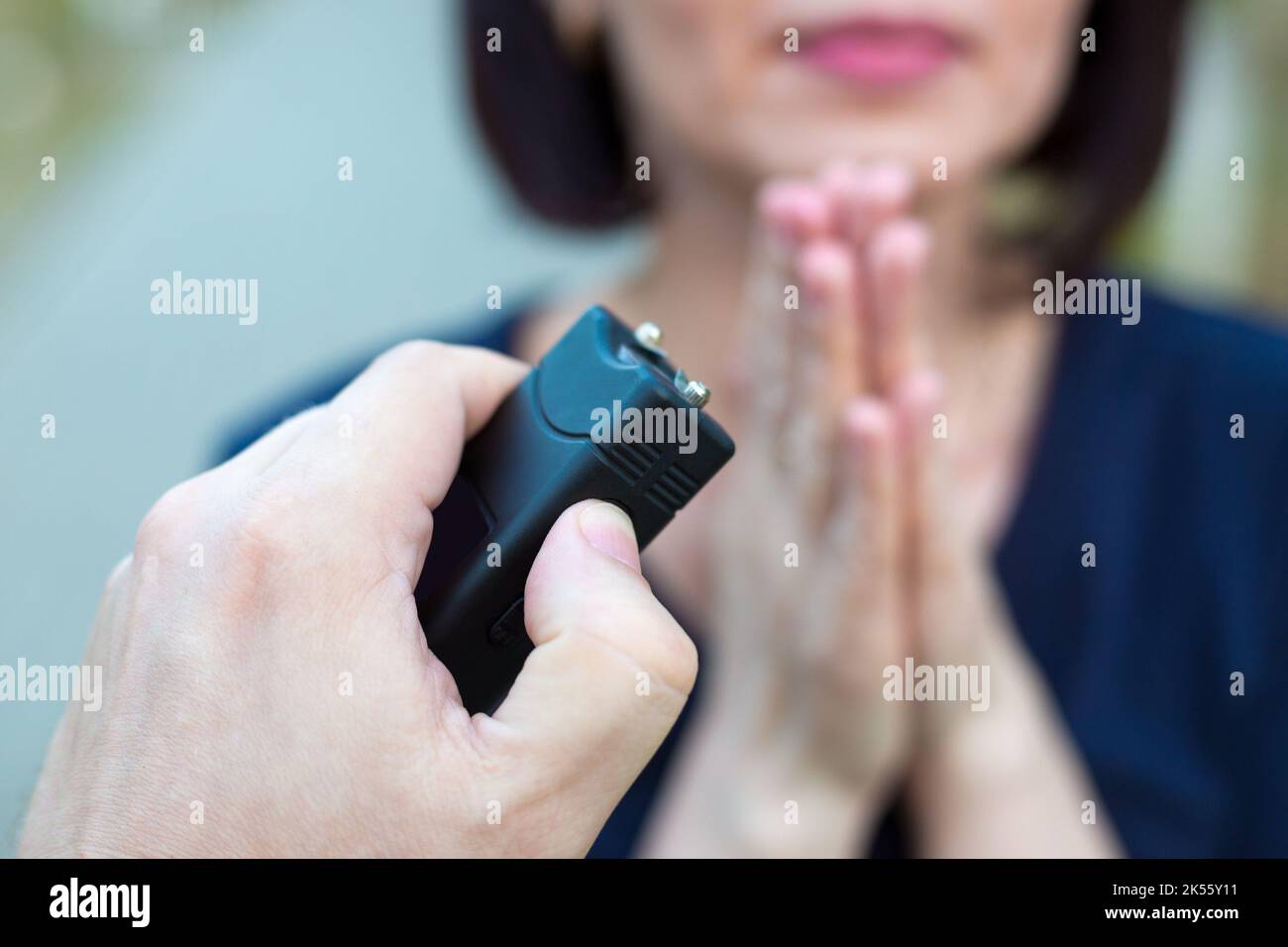 Frau, die vor einem Verbrecher mit einem Elektroschocker um Gnade bittet. Stockfoto