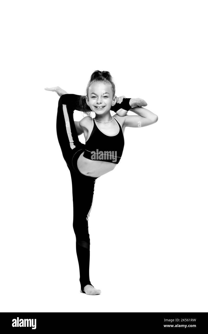 Eine junge, flexible Mädchengymnastin in einem Trainingsanzug macht gymnastische Stretching-Übungen. Sie warf ihr Bein über ihren Kopf. Schwarzweiß-Foto auf weißem Hintergrund. Hochwertige Fotos Stockfoto