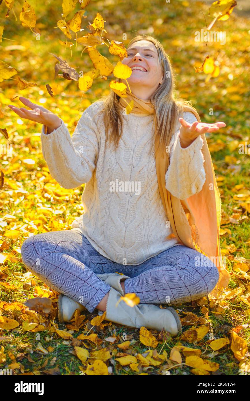 Im Herbst wirft eine junge Frau Blätter in einen Park Stockfoto