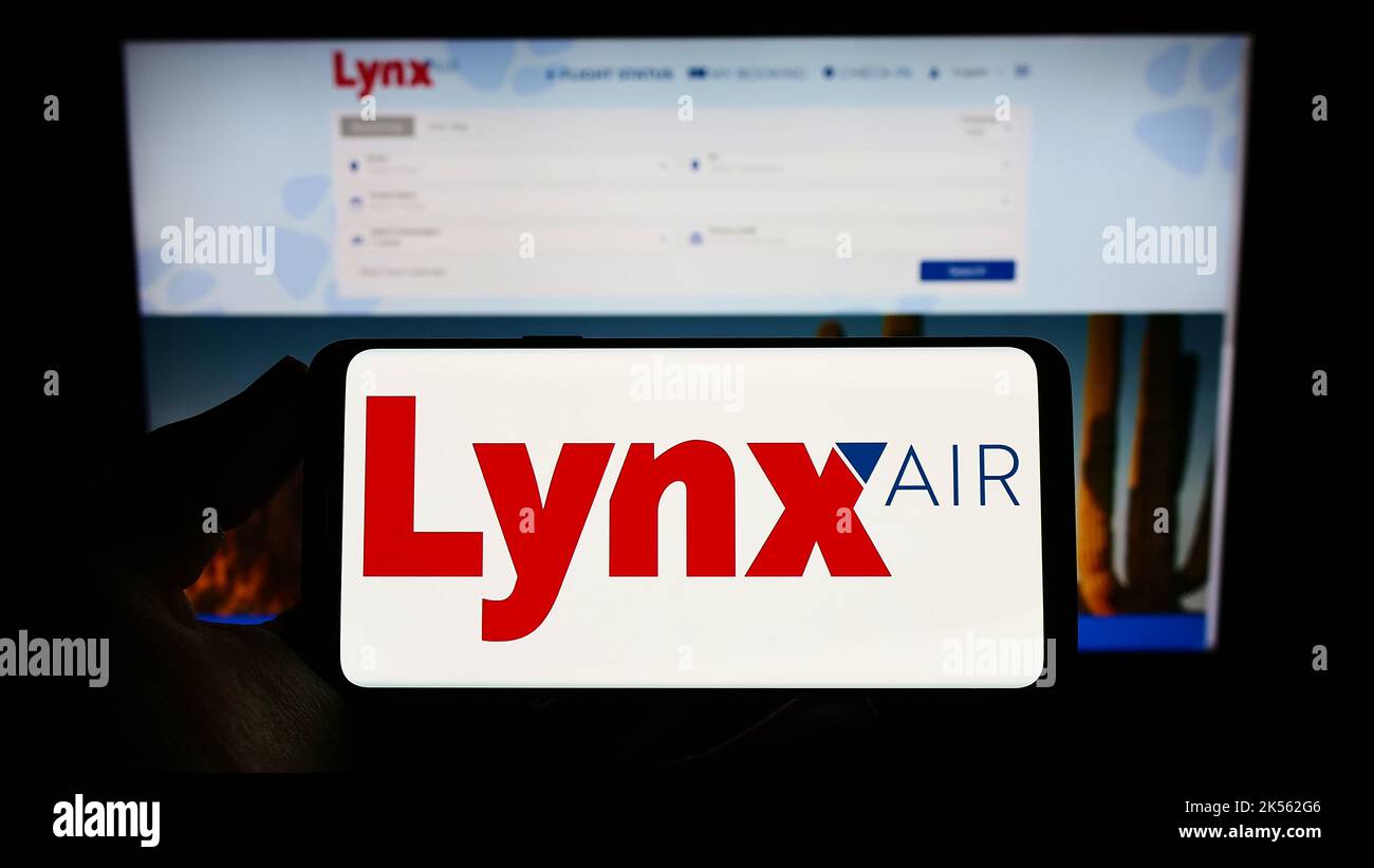 Person, die das Smartphone mit dem Logo der kanadischen Fluggesellschaft Lynx Air (1263343 Alberta Ltd.) auf dem Bildschirm vor der Website hält. Konzentrieren Sie sich auf die Telefonanzeige. Stockfoto
