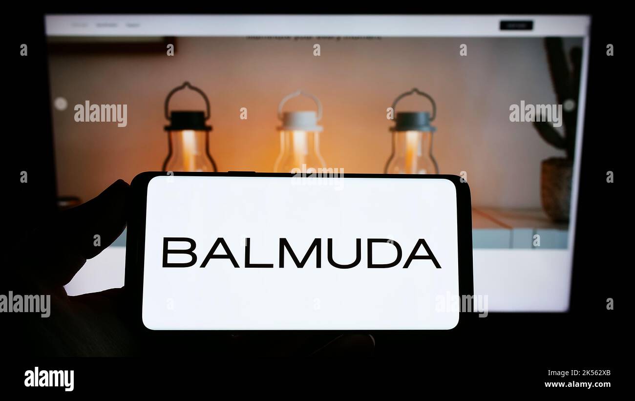 Person, die Mobiltelefon mit Logo des japanischen Designunternehmens BALMUDA K.K. auf dem Bildschirm vor der Business-Webseite hält. Konzentrieren Sie sich auf die Telefonanzeige. Stockfoto