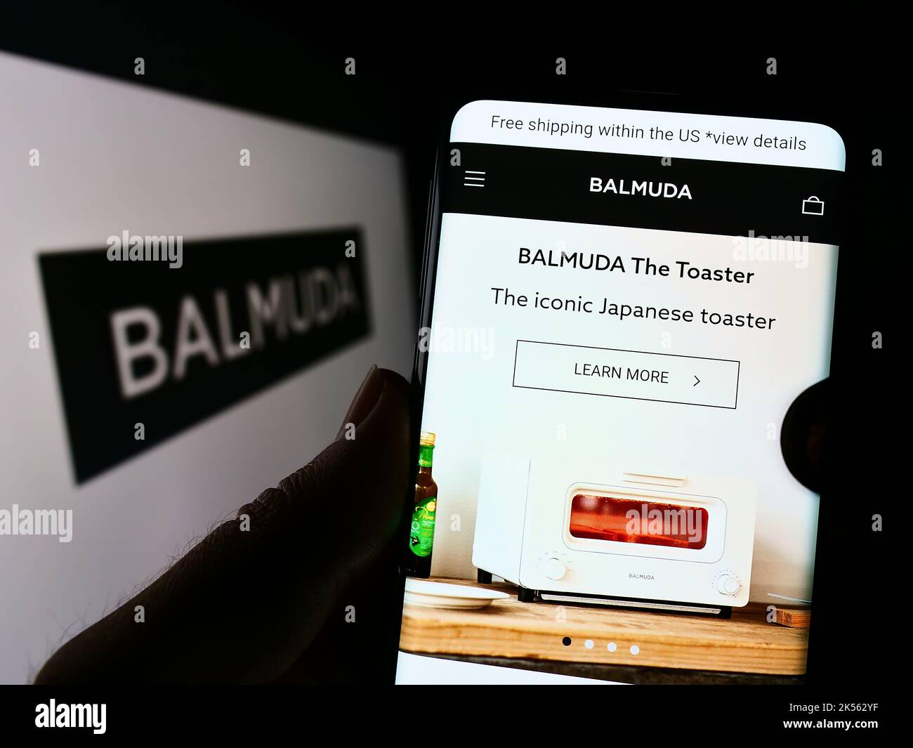 Person, die Mobiltelefon mit der Website des japanischen Designunternehmens BALMUDA K.K. auf dem Bildschirm vor dem Logo hält. Konzentrieren Sie sich auf die Mitte des Telefondisplays. Stockfoto