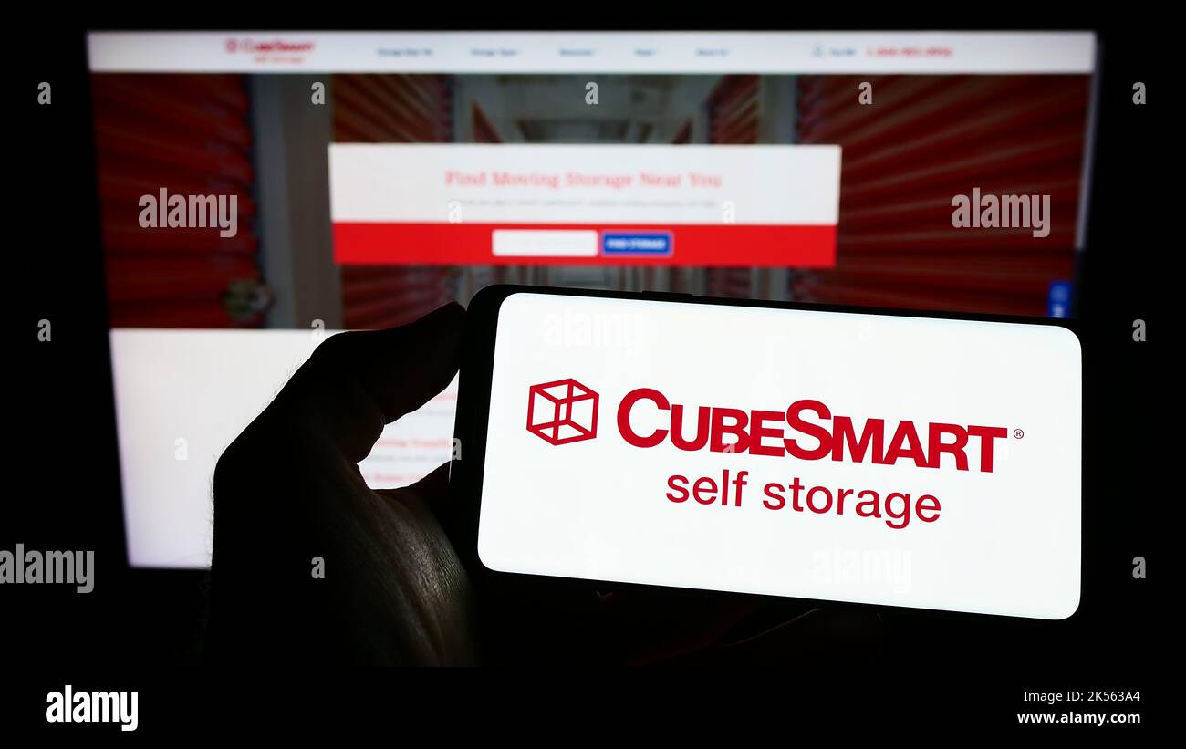 Person, die Mobiltelefon mit dem Logo des US-amerikanischen Selfstorage-Unternehmens CubeSmart auf dem Bildschirm vor der Business-Webseite hält. Konzentrieren Sie sich auf die Telefonanzeige. Stockfoto