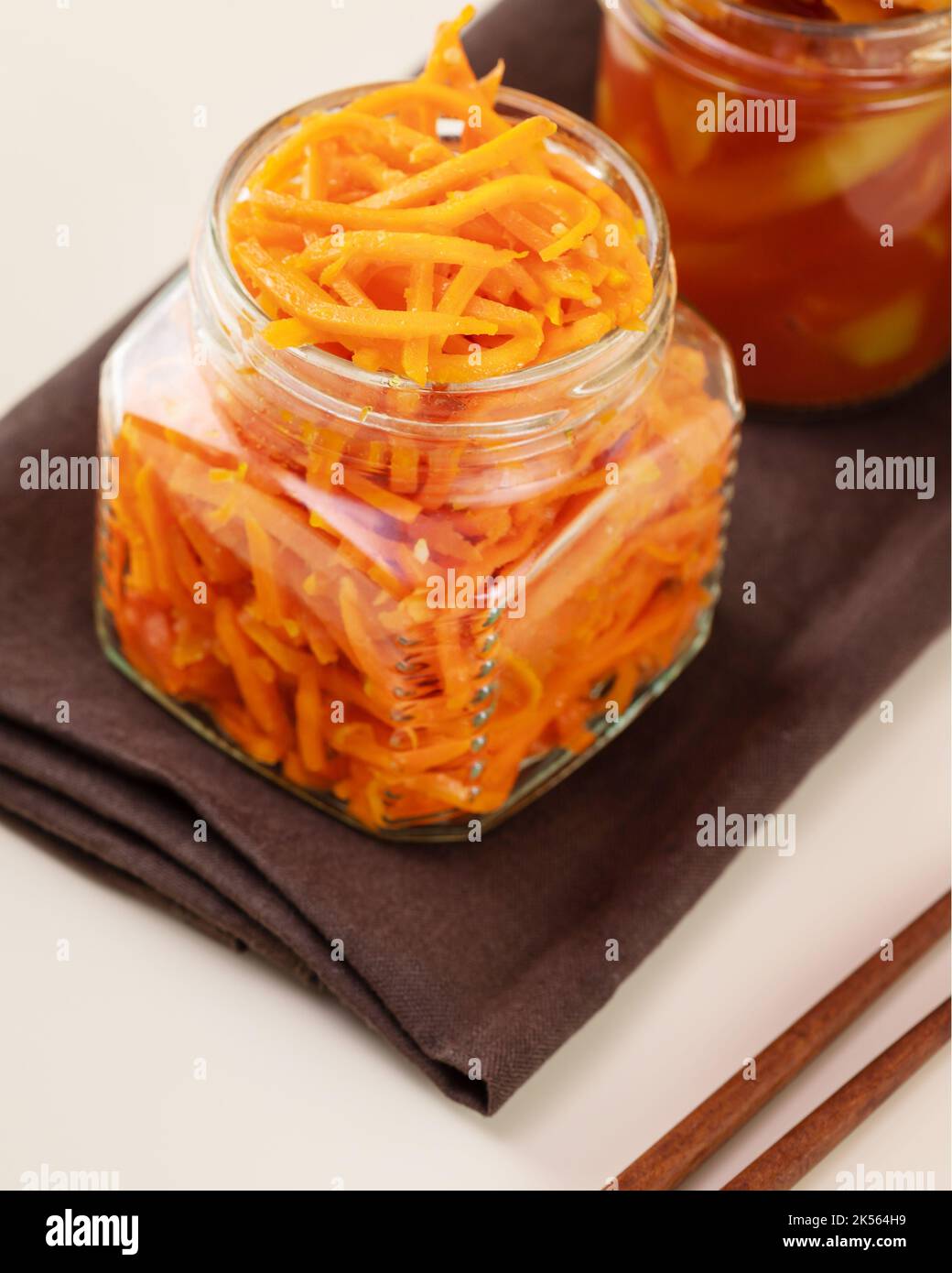 Koreanische Karotte im Glas auf einer braunen Serviette mit Essstäbchen Stockfoto