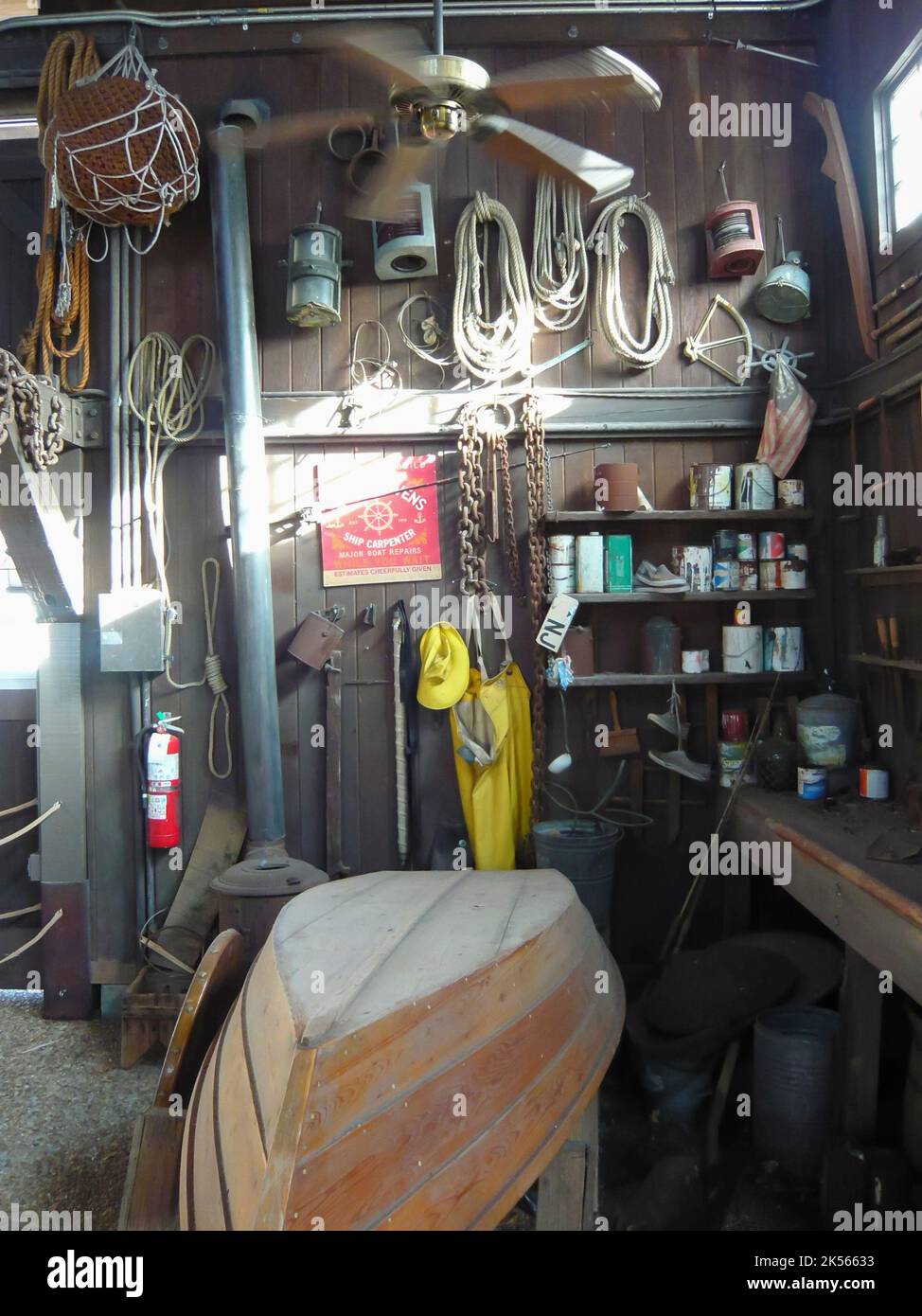 Im Inneren einer Bootsbau- und Reparaturwerkstatt mit einem umgedrehten Ruderboot, Seilen, Farbdosen und Werkzeugen. Stockfoto