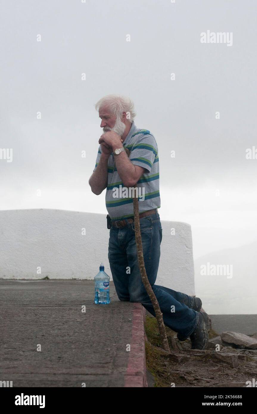 Ein Mann kniet am Reek-Sonntag auf dem Gipfel des Croagh Patrick vor der Kirche, als römisch-katholische Pilger auf den Gipfel steigen, um den Stufen des heiligen Patrick zu folgen. Stockfoto