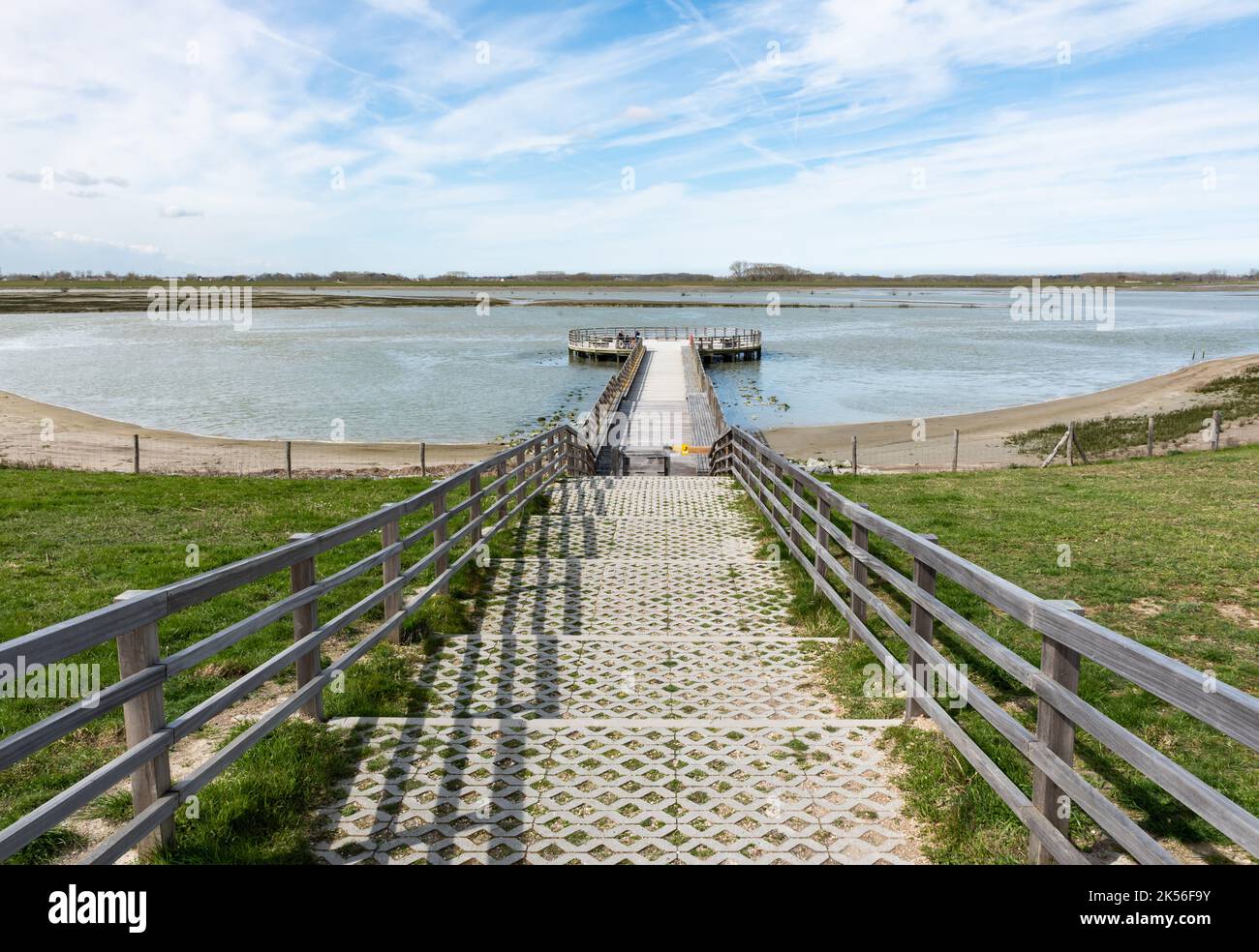 Knokke Heist, Flämische Region - Belgien - 04 03 2021 Aktive Frau, die einen hölzernen Pier in einem Naturschutzgebiet am Meer entlang läuft Stockfoto