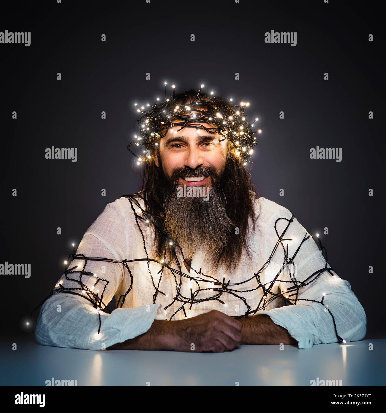 Mann mit Bart und langen Haaren lächelt mit weihnachtslichtern Stockfoto