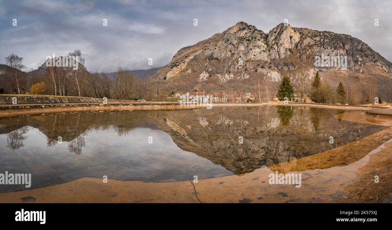 Berggipfel und Bäume spiegeln sich in einem künstlichen Teich. Surba Stadt versteckt sich hinter Bäumen am Fuße der Pyrenäen Tarascon sur Ariege Frankreich Stockfoto
