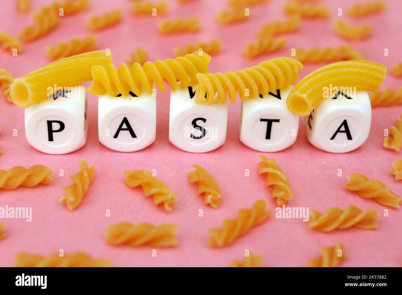 Verschiedene rohe, ungekochte Pasta mit Buchstaben, die das Wort Pasta auf einem rosa Hintergrund wie ein grafisches Konzept von Pasta erzeugen Stockfoto