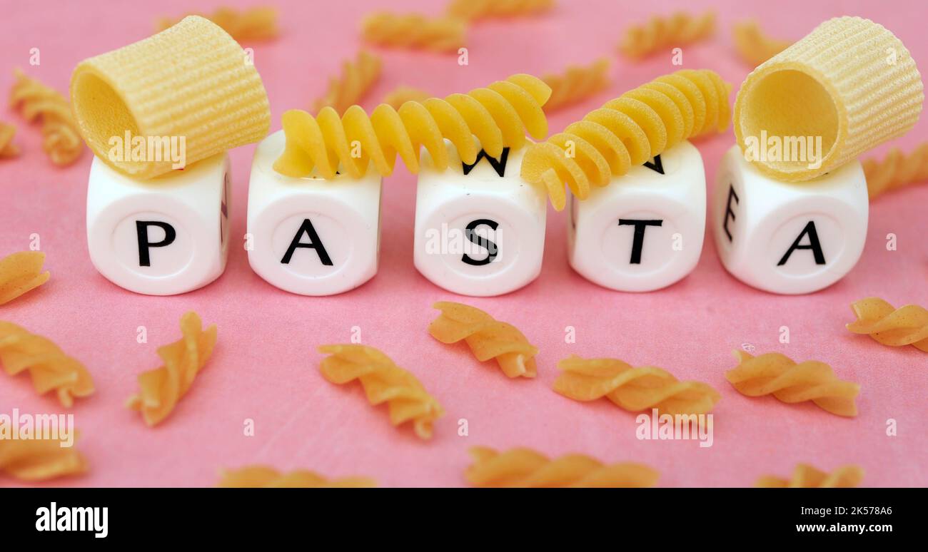 Verschiedene rohe, ungekochte Pasta mit Buchstaben, die das Wort Pasta auf einem rosa Hintergrund wie ein grafisches Konzept von Pasta erzeugen Stockfoto