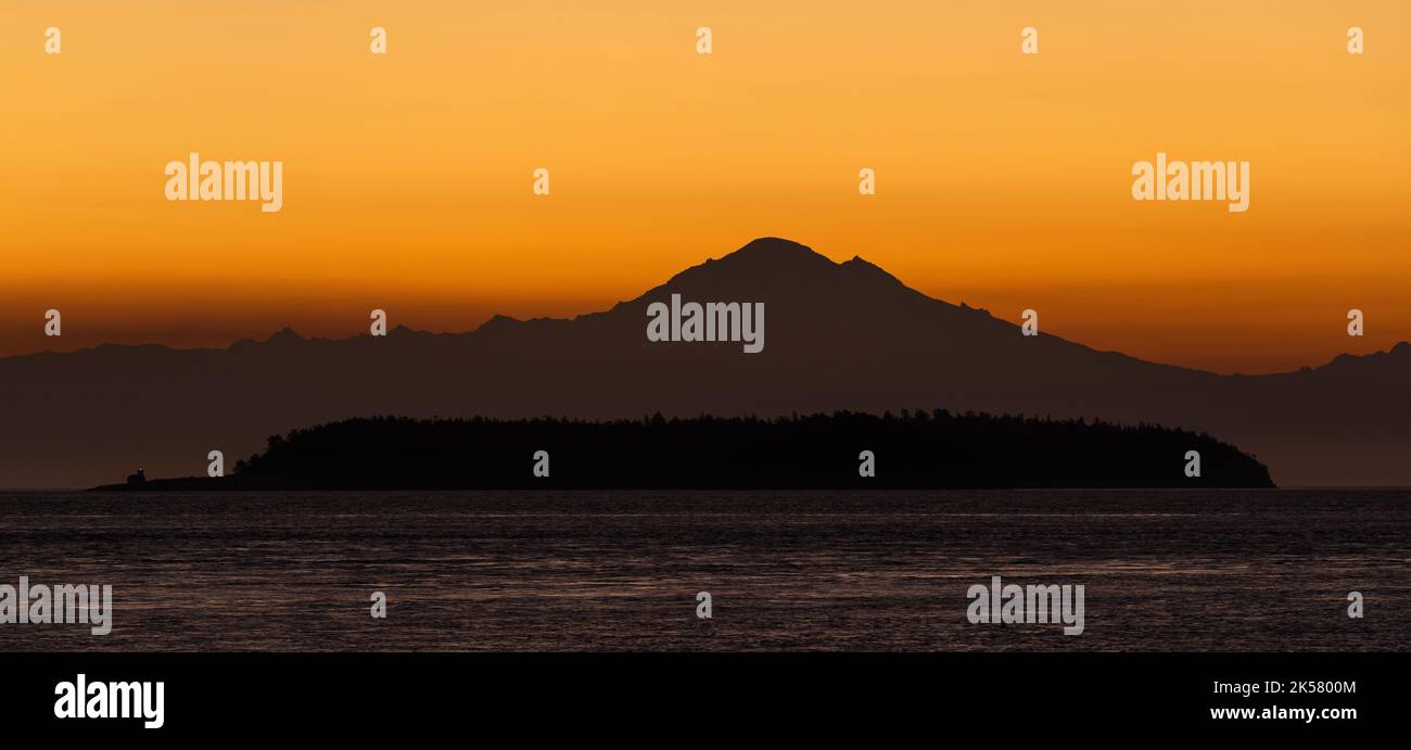 Hinter Mount Baker und Patos Island, von Saturna Island in British Columbia, Kanada aus gesehen, erleuchtete sich ein Morgenhimmel. Stockfoto