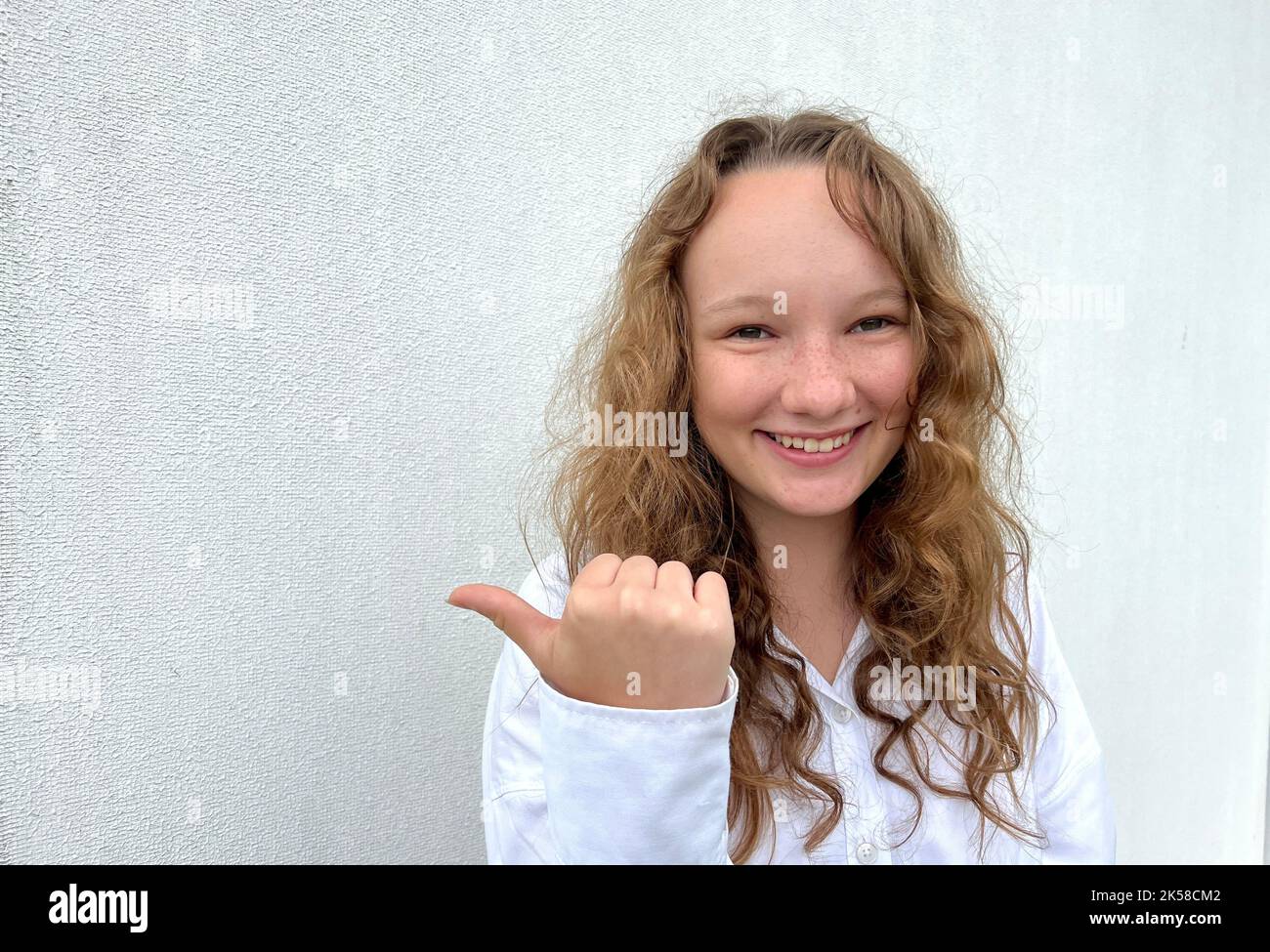 Ein Mädchen auf weißem Hintergrund in einer weißen Bluse, hellhaarig, zeigt andere fröhliche Emotionen, sie macht Gesichter, sie lacht fröhlich, sie kräuselt ihre Haare und zeigt ihre Zunge. Hochwertige Fotos Stockfoto