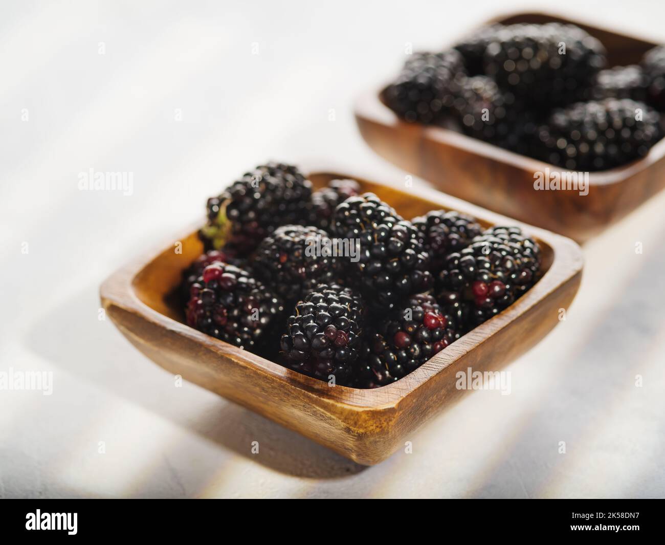 Auf weißem Hintergrund zwei Holzschalen mit Beeren von reifen duftenden Brombeeren. Köstliche gesunde Dessert, Vitamine, Antioxidantien. Kochen ist ein i Stockfoto