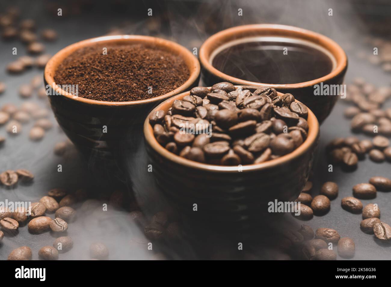 Tassen Kaffee unter ausgewählten und kalibrierten Arabica-Kaffeebohnen, verteilt auf schwarzem Hintergrund, drei aromatische Tassen Kaffee in einem Paar. Stockfoto