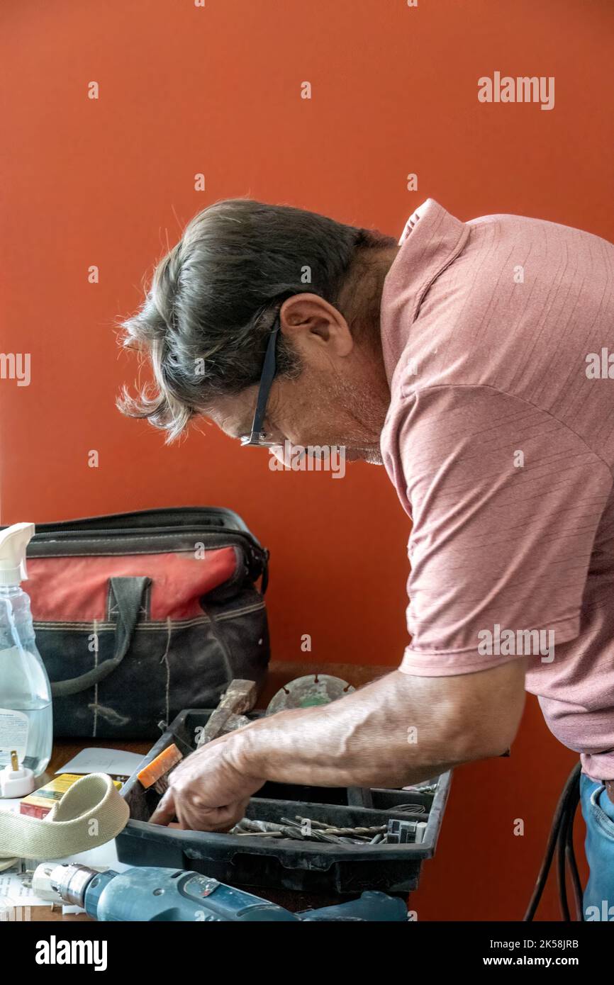 lateinamerikanischer Mann, der nach Werkzeugen in seiner Werkzeugkiste sucht, mit Schraubendreher in der Hand Stockfoto