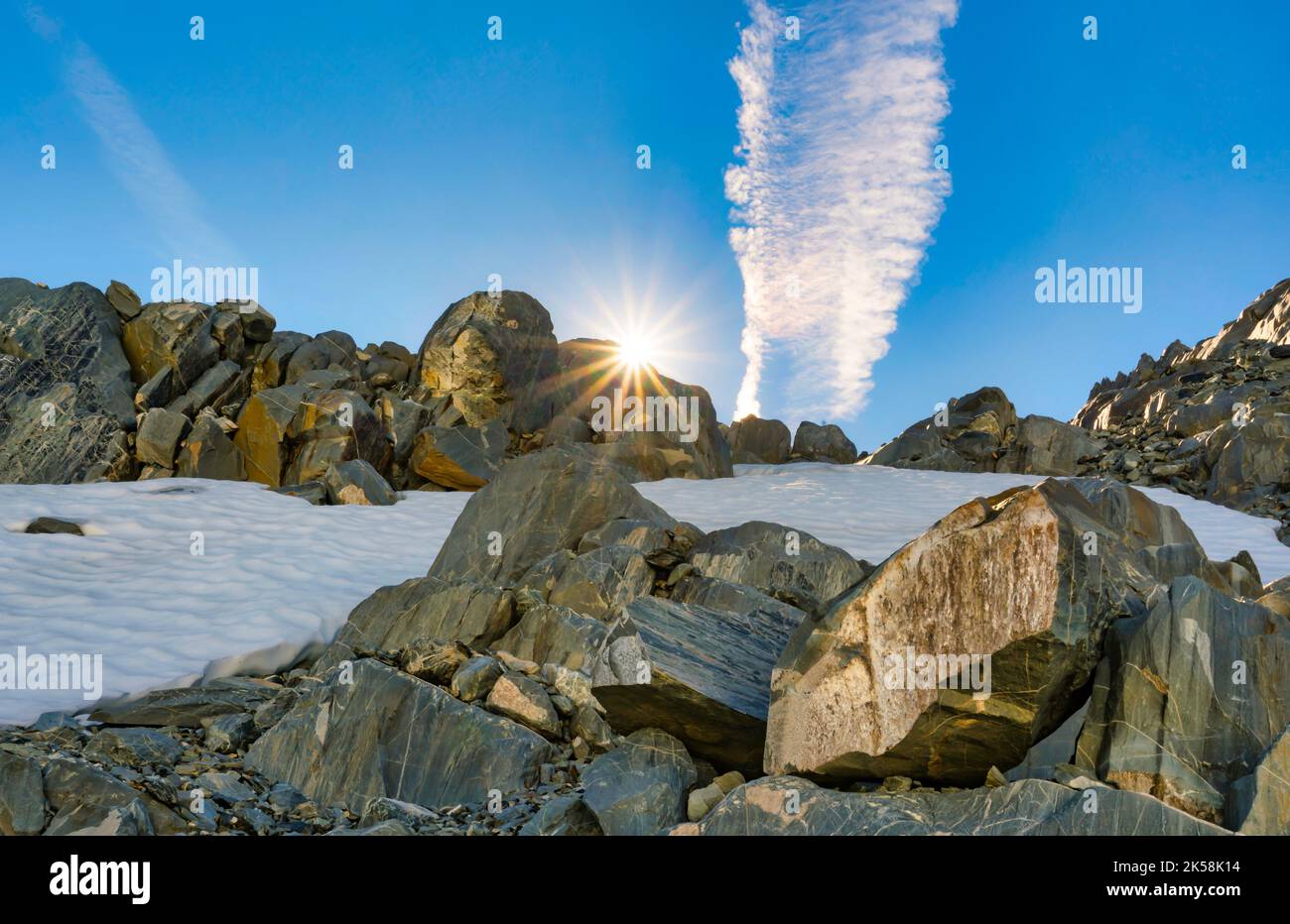 Sun Flare hinter den Felsen und chem Trail wie Wolkenformationen hoch in den Südalpen auf einem alpinen Gletscher Stockfoto