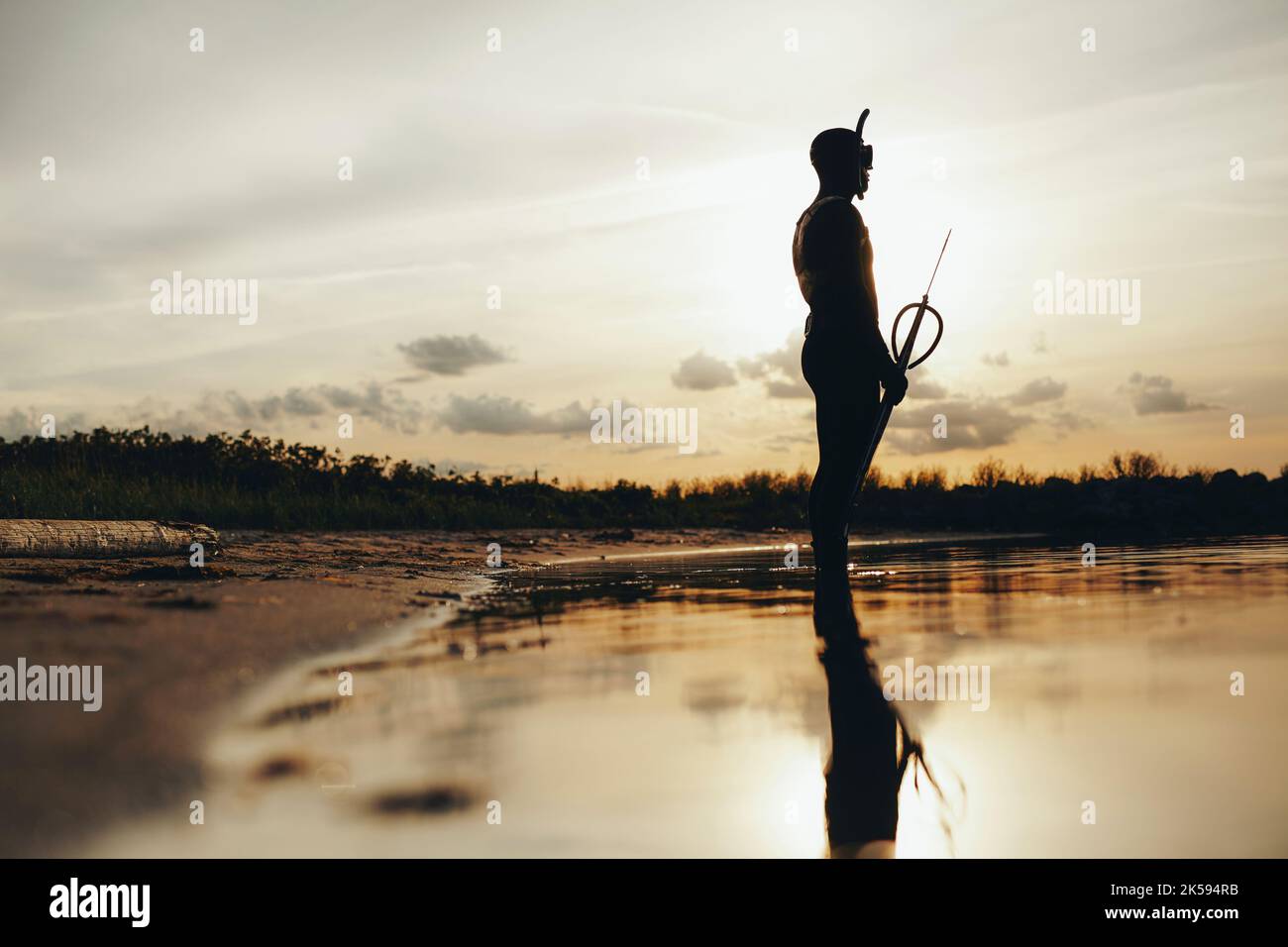 Seitenansicht des Speerfischers, der bei Sonnenuntergang Speerfischen geht. Silhouette eines abenteuerlichen Tauchers, der im Meerwasser mit einer Speerpistole in der Hand steht. Stockfoto