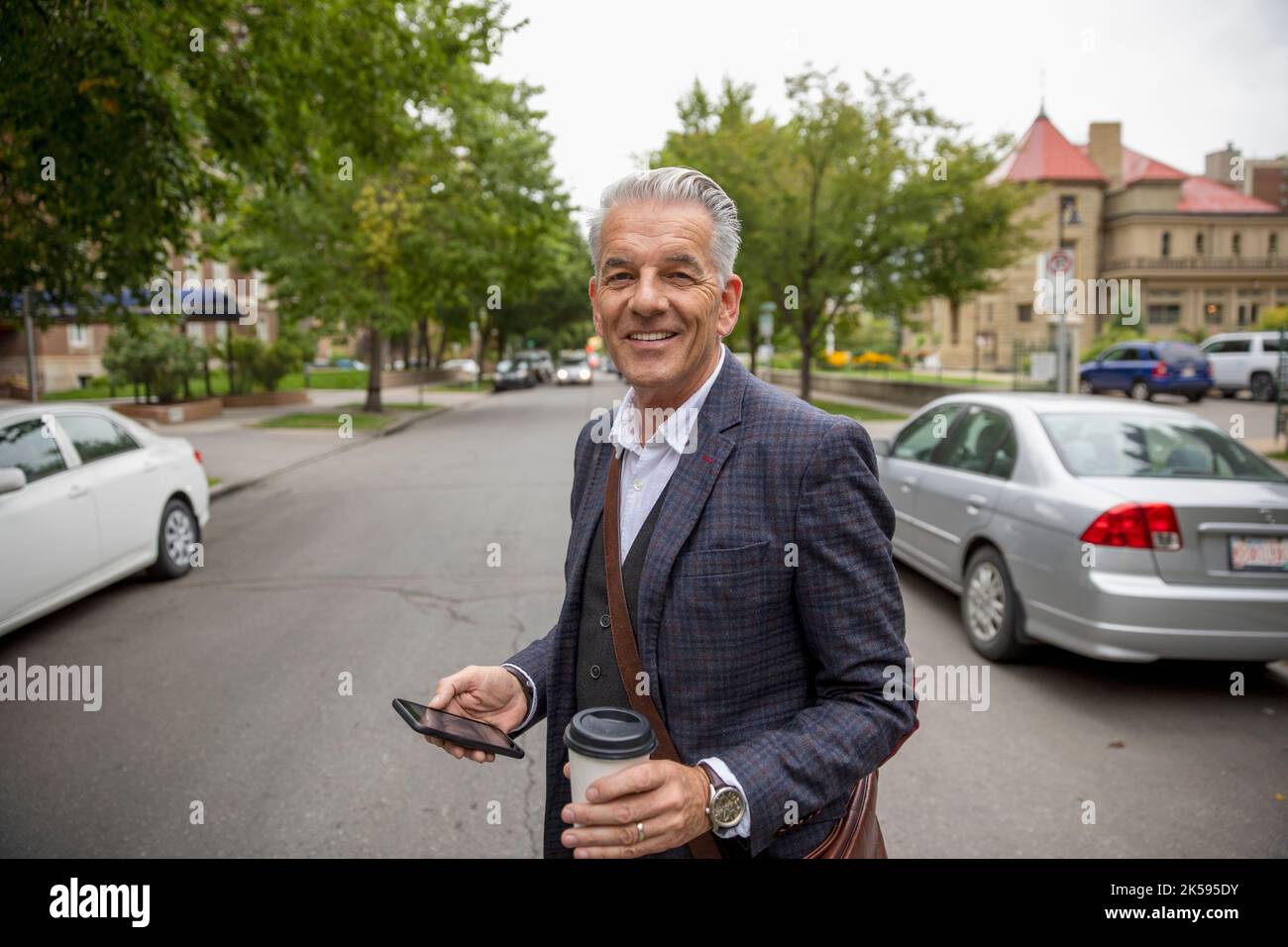 Porträt selbstbewusster, lächelnder Geschäftsmann mit Kaffee und Smartphone auf der Straße der Stadt Stockfoto