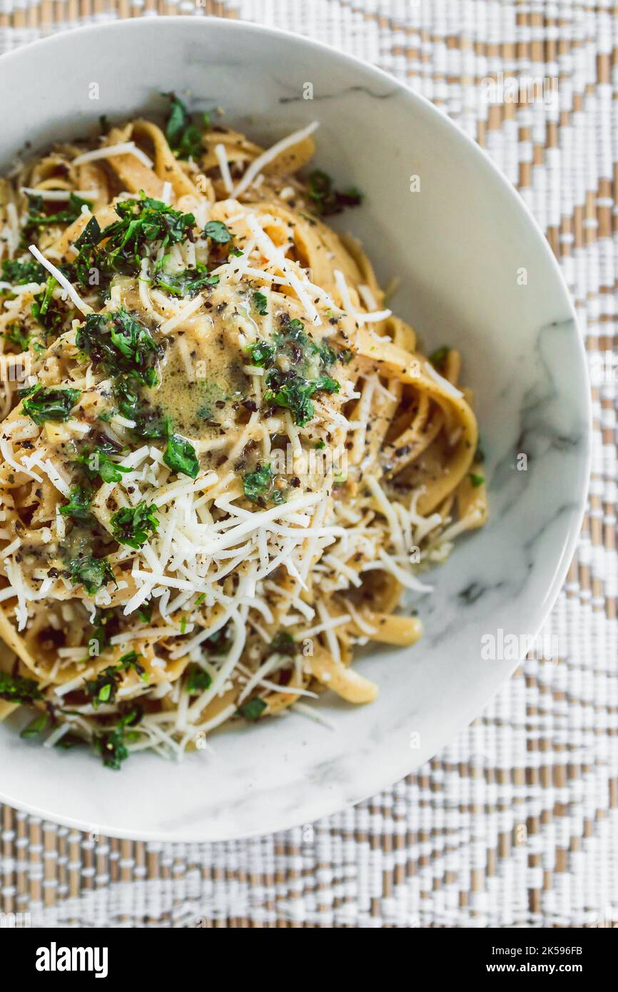 Fettuccini-Pasta auf pflanzlicher Basis mit cremiger Zitronen- und Petersiliensauce, gekrönt mit frischen Kräutern und milchfreiem Käse, gesunden veganen Rezepten Stockfoto