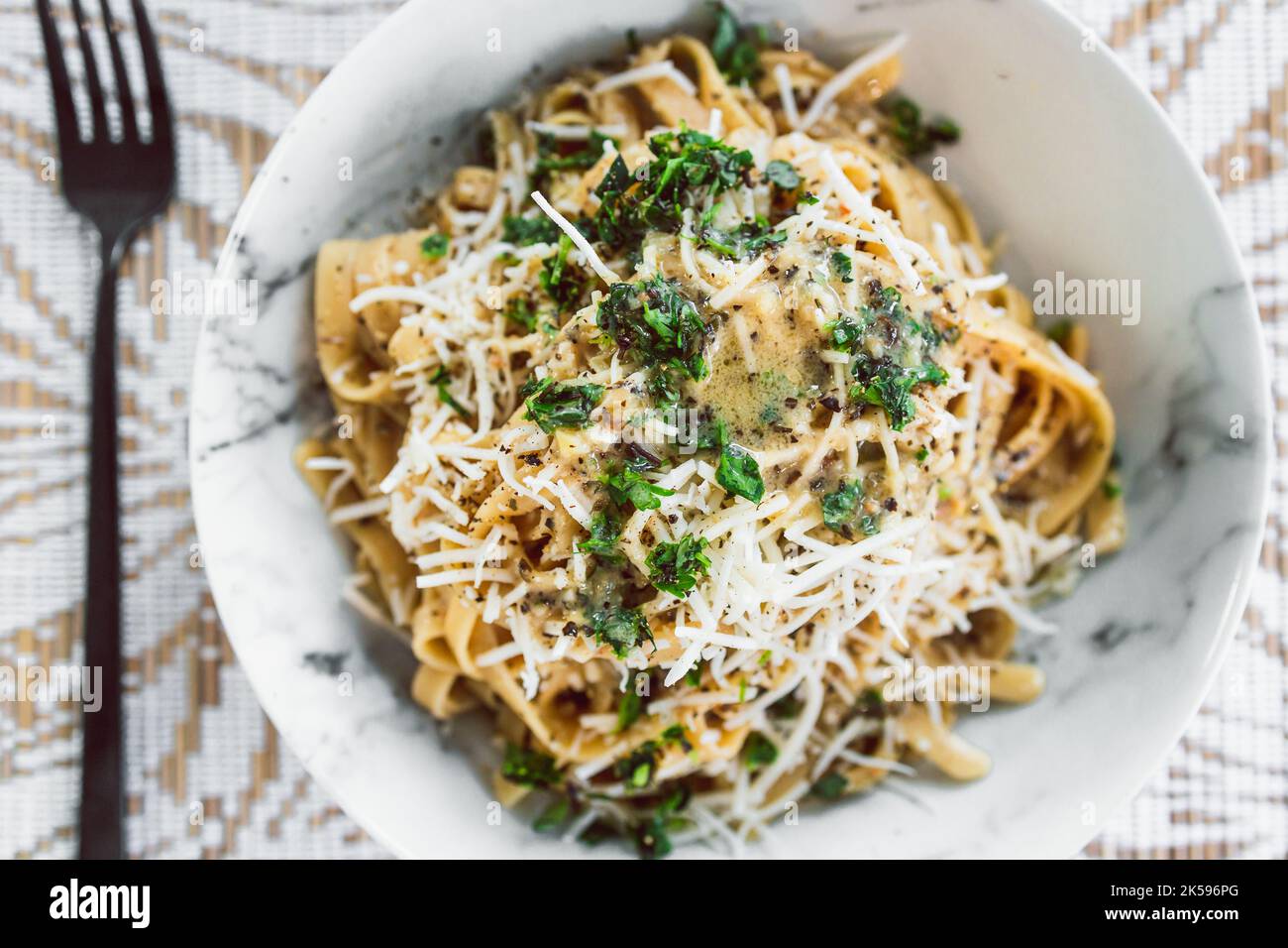 Fettuccini-Pasta auf pflanzlicher Basis mit cremiger Zitronen- und Petersiliensauce, gekrönt mit frischen Kräutern und milchfreiem Käse, gesunden veganen Rezepten Stockfoto