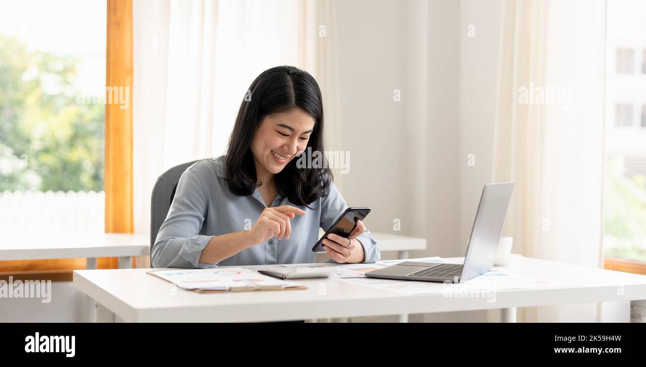 Geschäftsfrau oder Buchhalter Hand mit Handy-Smartphone und Laptop-Computer mit dokumentarischen Daten Graph Papier auf dem Tisch im modernen Home Office Stockfoto