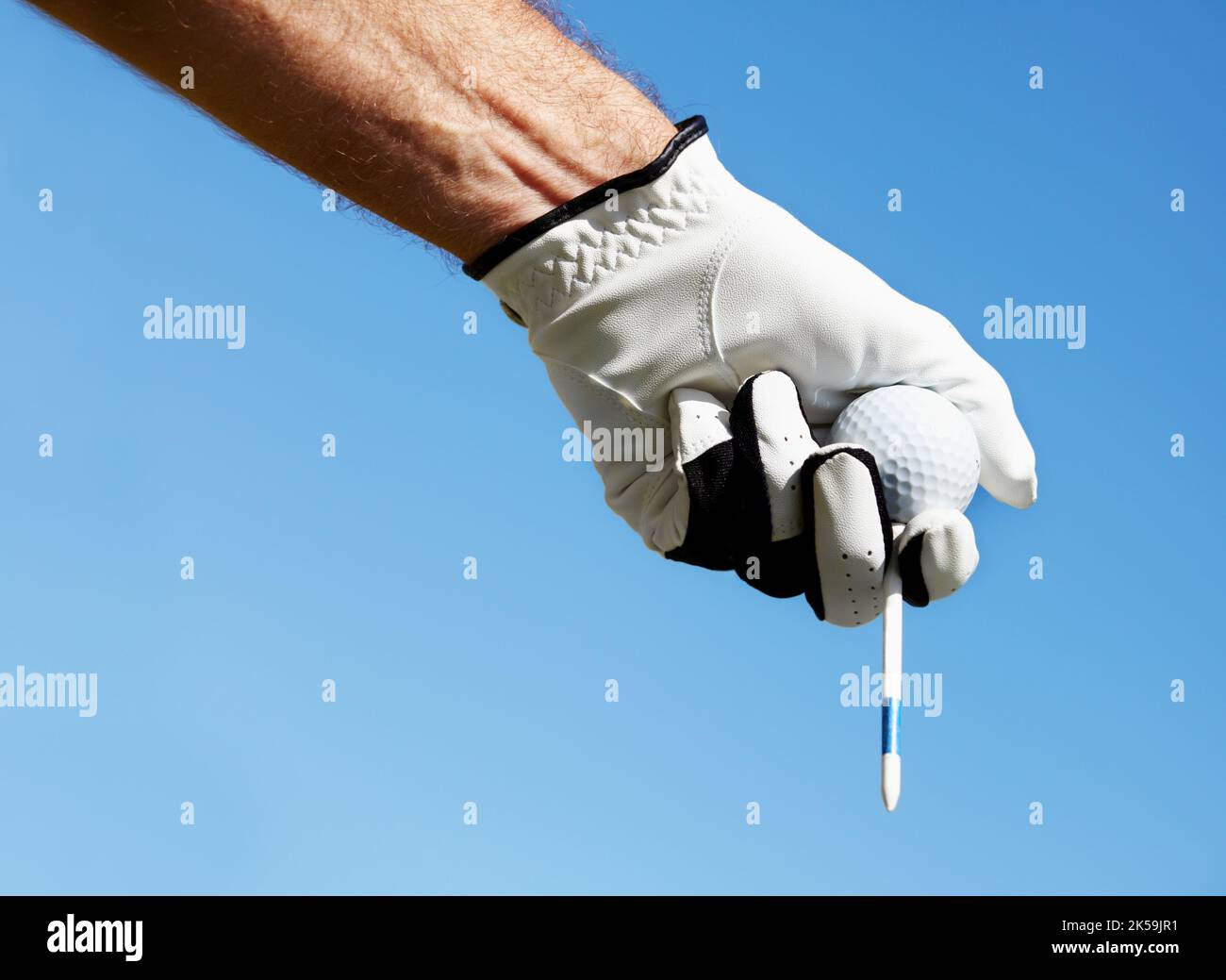 Der Himmel ist die Grenze, wenn du hart genug übst. Ein Golfer hält sein T-Shirt und seinen Golfball gegen einen blauen Himmel. Stockfoto