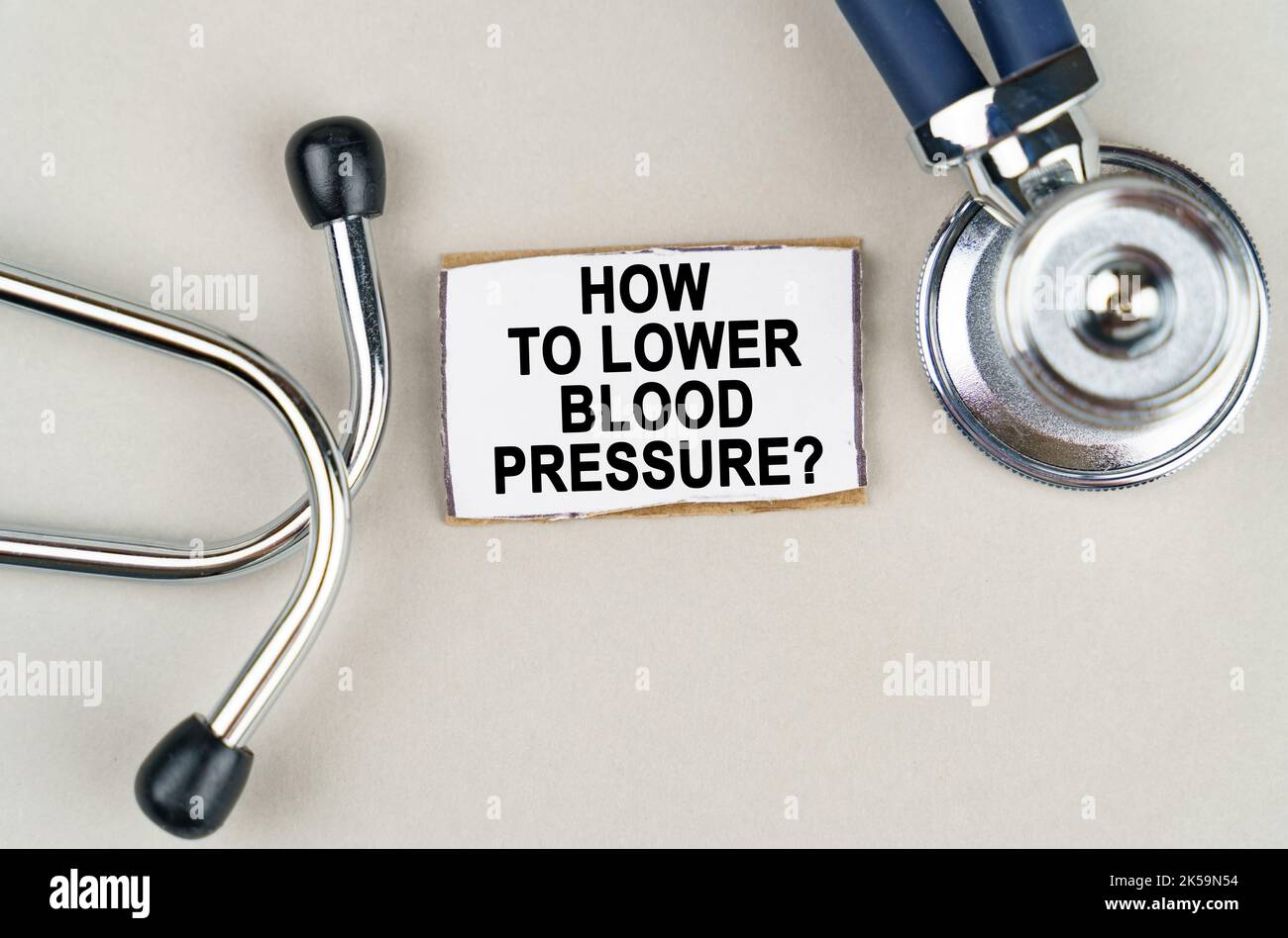 Medizinisches Konzept. Auf grauem Hintergrund ein Stethoskop und ein Pappschild mit der Aufschrift - wie man den Blutdruck senkt Stockfoto