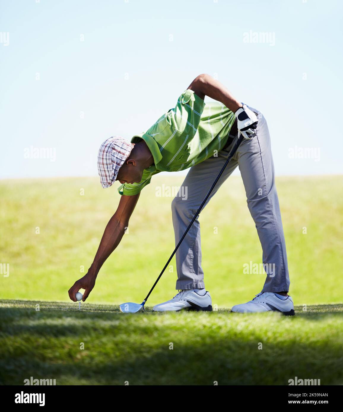 Platzieren seines Balls für den letzten Antrieb. Ein junger afroamerikanischer Golfer platziert seinen Golfball auf einem Abschlag. Stockfoto