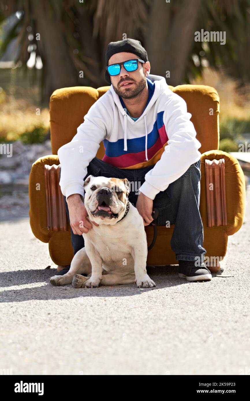 Mein bester Freund. Ein trendiger Rüde, der auf einer Couch auf der Straße mit Hund und Sonnenbrille sitzt. Stockfoto