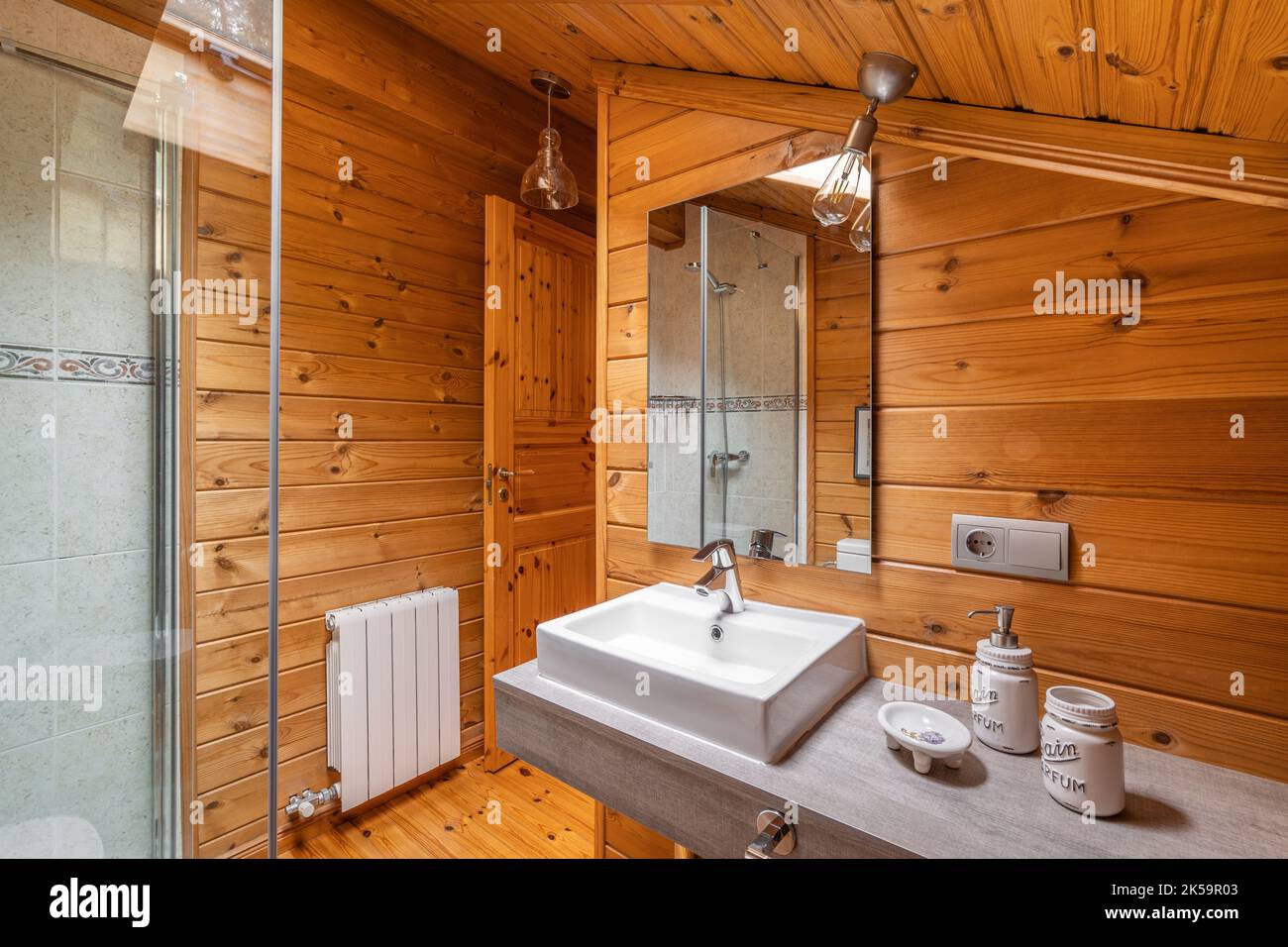 Die Einrichtung des Badezimmers im Landhausstil mit Holzwänden. Duschkabine und Waschbecken mit Spiegel Stockfoto