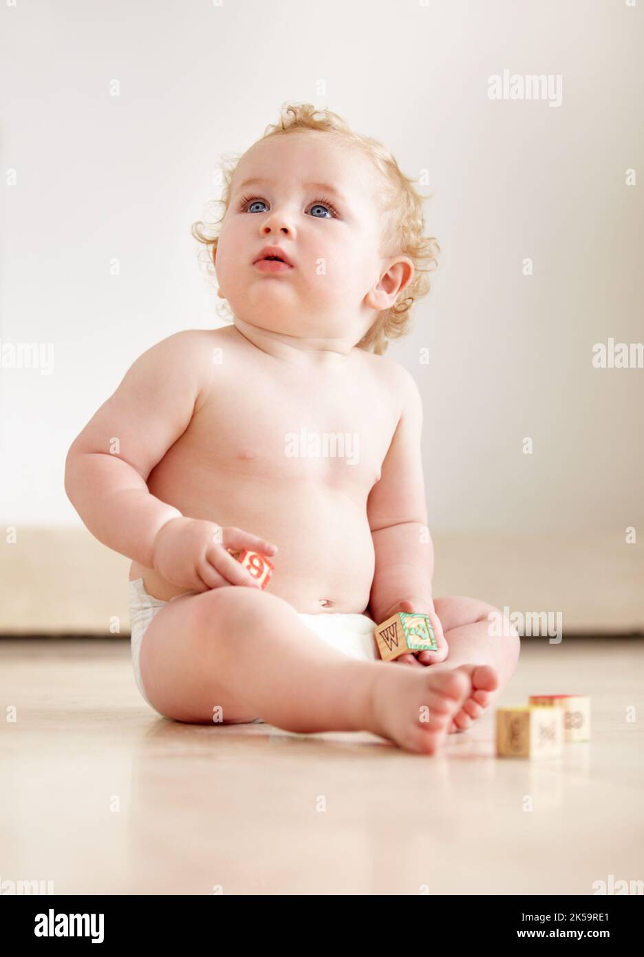 Was ist das da oben - kindliche Kuriousität. Niedlicher Junge schaut neugierig auf, während er auf dem Boden sitzt. Stockfoto