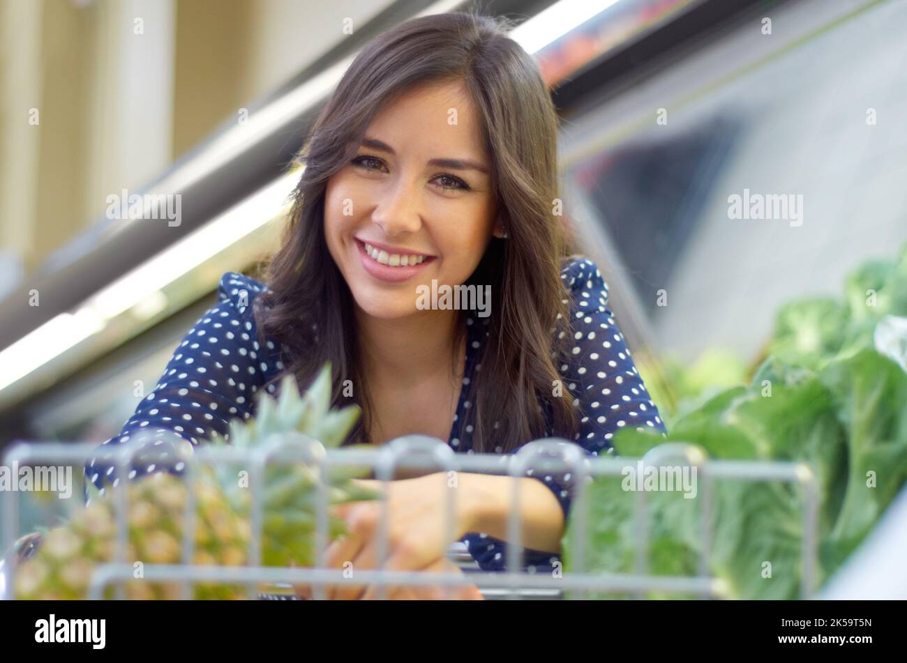 Ich und mein Gemüse. Eine junge Frau, die mit ihrem Einkaufswagen lächelt. Stockfoto