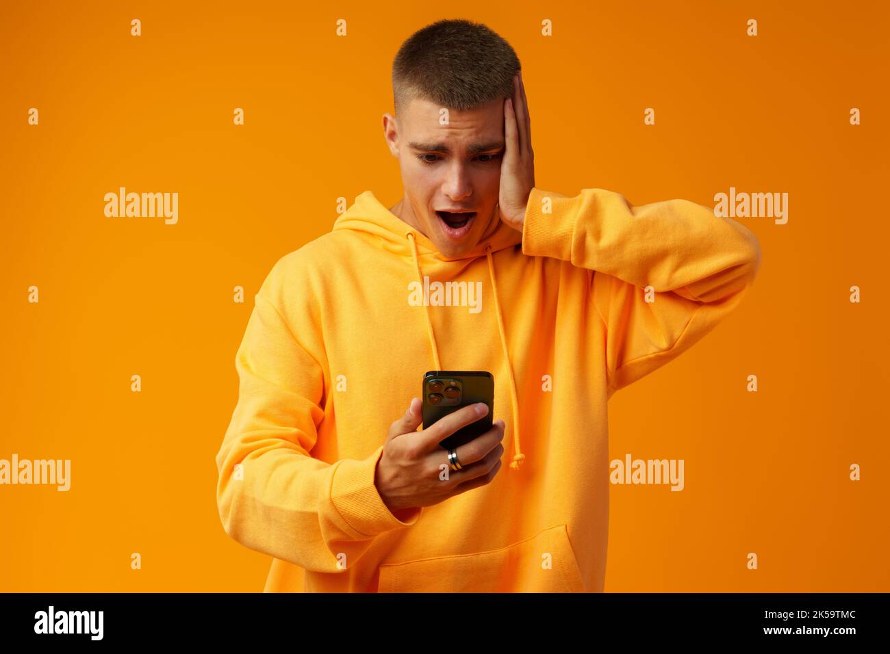 Junger Mann, der Negativität ausdrückt, während er die Nachricht auf dem Mobiltelefon auf gelbem Hintergrund liest Stockfoto