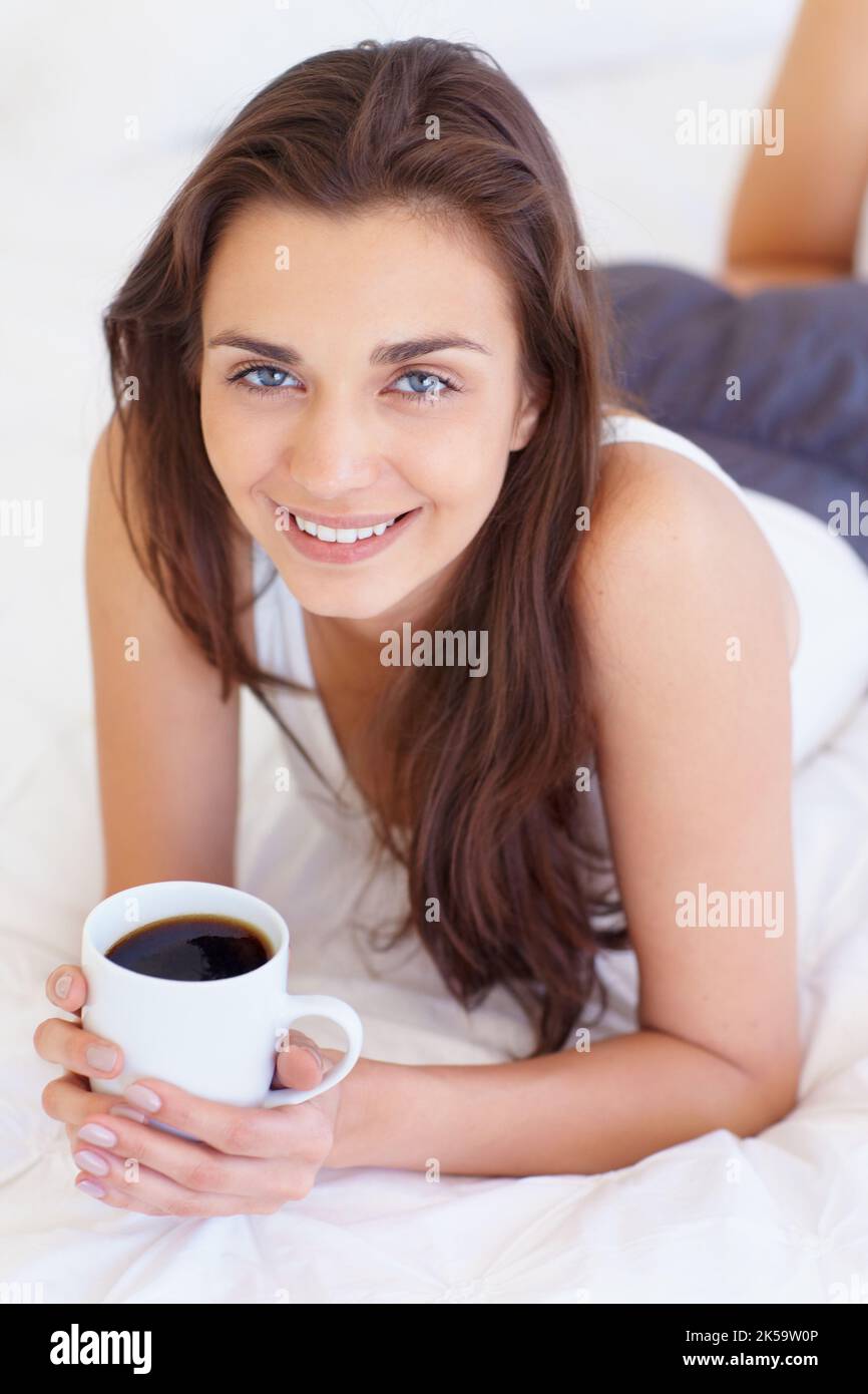 Mein Morgenkaffee. Porträt eines lächelnden hübschen Teenagers, das sich mit einem heißen Getränk in der Hand auf ihrem Bett entspannt. Stockfoto