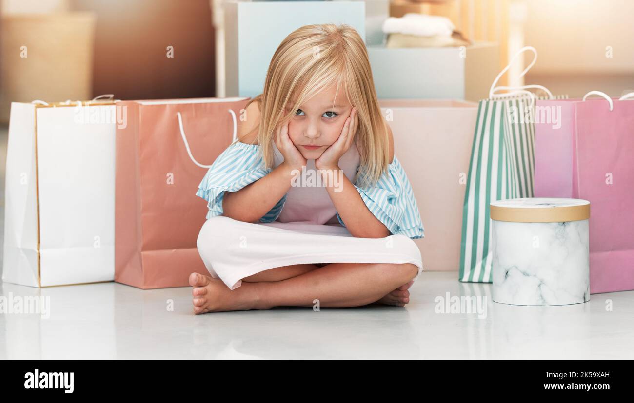 Gelangweiltes Kind, Mode und Einkaufstaschen warten auf dem Boden in Kinderkleidergeschäft, Geschäft oder Boutique mit niedlichen Mädchen sitzen aufgeregt suchen. Kinderportrait Stockfoto