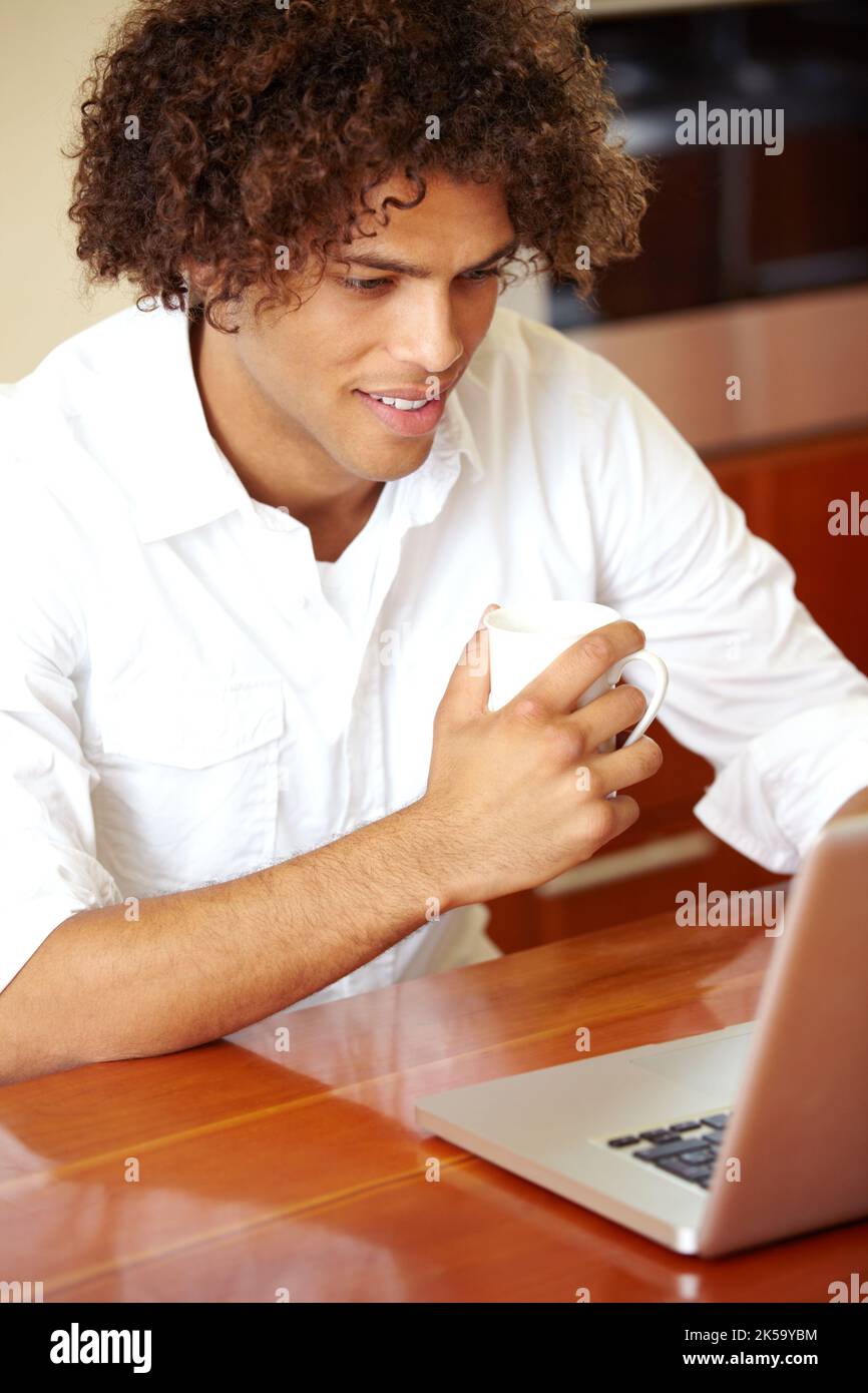 Nachholen, was vor sich geht. Ein junger Mann, der Kaffee trinkt, während er im Internet surft. Stockfoto
