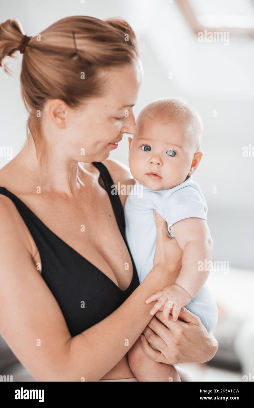 Porträt eines süßen Babys, das in den Armen der Mutter ruht und die Kamera anschaut. Neue Mutter hält und kuschelt kleines Kind, umarmt Kind mit Zärtlichkeit, Liebe Stockfoto