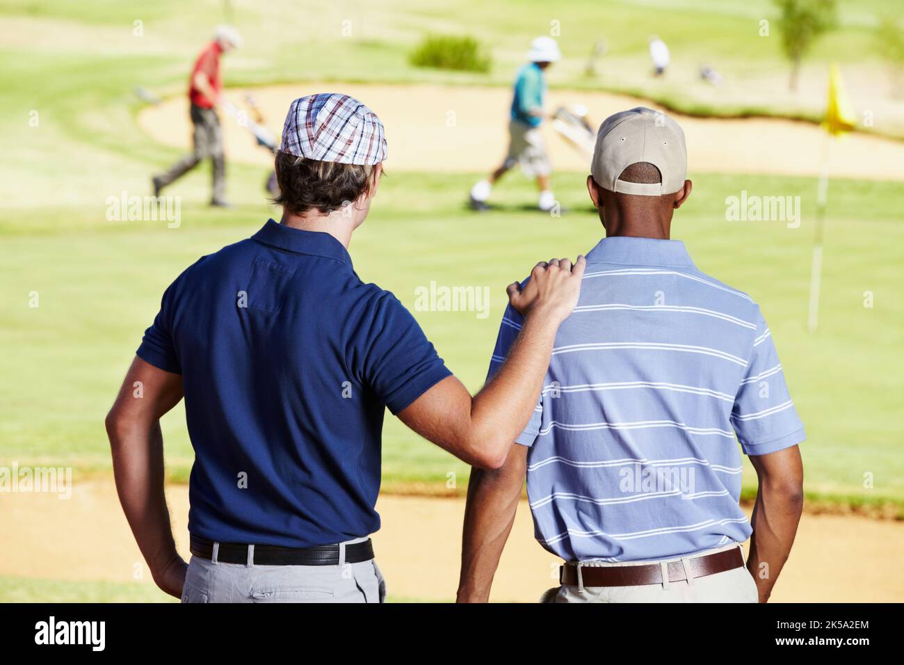 Warten auf das Loch. Rückansicht von zwei Freunden, die eine Gruppe von Golfern in der Ferne beobachten. Stockfoto