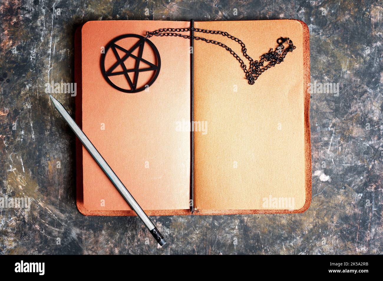 Notizbuch aus braunem Leder mit Bleistift und schwarzer Pentagramm-Halskette auf dunklem grünem Hintergrund. Kreatives Spell Book Konzept. Stockfoto
