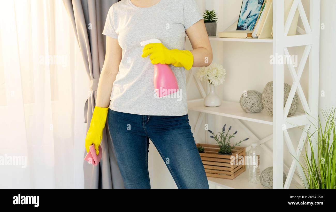 Reinigungswerkzeuge. Hausarbeit Routine. Hausarbeiten. Unkenntlich Frau in gelben Handschuhen Jeans T-Shirt hält Waschmittel Spray und Mikrofaser Tuch Licht Stockfoto