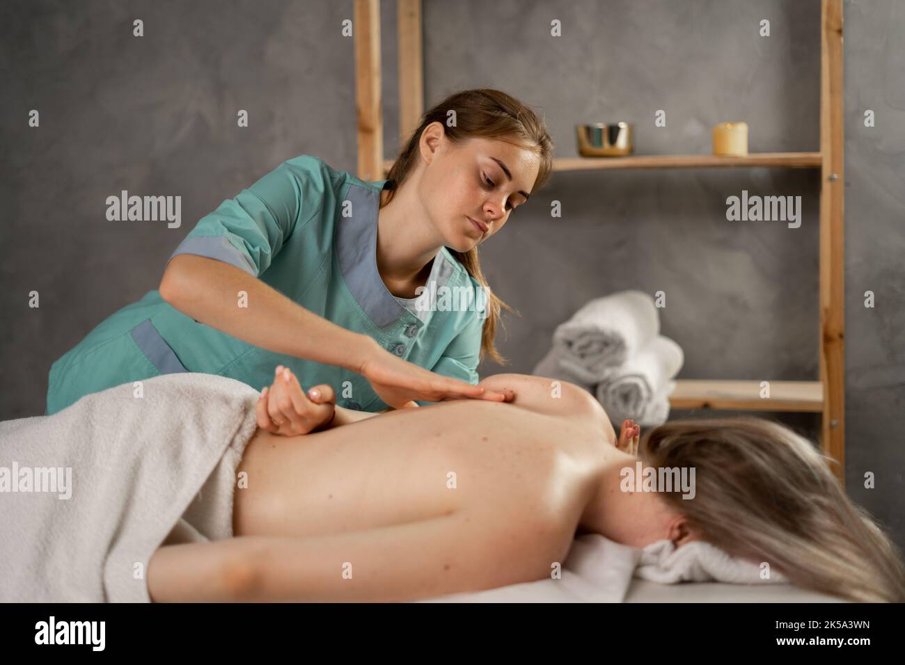 Professionelle Masseurin oder manuelle Therapeutin massiert die Schulter einer jungen Frau und lindert so die Schmerzen. Weibliche Patientin erhält Heilkörpermassage in der Physiotherapie Stockfoto